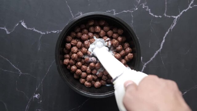  Top view of pouring milk on chocolate corn flakes in a bowl 