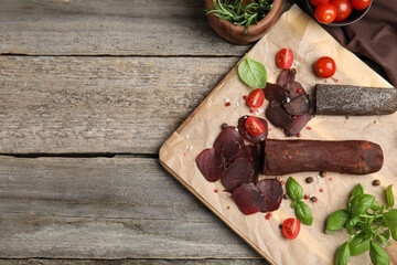Delicious dry-cured beef basturma with basil, tomatoes and spices on wooden table, flat lay. Space for text