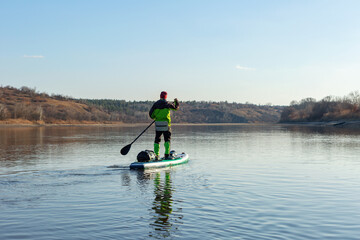 Fototapeta na wymiar Late autumn on a clear day a man is rafting on a supboard on the river. SUP