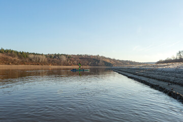 Late autumn on a clear day a man is rafting on a supboard on the river. SUP