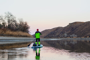 A man is rafting on the river on a supboard in the late autumn in the evening, looking into the distance at the mountains. SUP