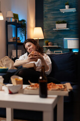 Woman enjoying phone conversation and having fast food delivery dinner relaxing on couch in living room after work. Office worker talking on smartphone with friends while holding tasty delicious