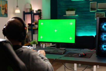 Player looking at computer with horizontal green screen. Man using isolated template and mockup background with chroma key to play video games on monitor. Gamer holding controller.