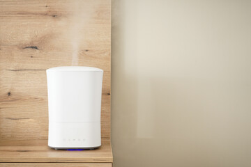 Modern air humidifier on the bedside table in the bedroom, space for text.