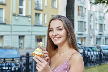 attractive girl with long hair holds a cake in her hands and spreads cream on her finger. photo shoot in the city