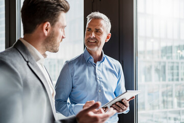 Mature male entrepreneur holding digital tablet discussing with colleague in meeting at office