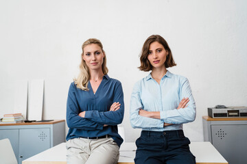 Young female professional sitting with arms crossed on desk in office