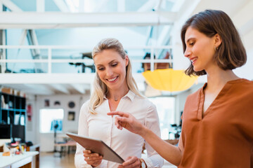 Young female entrepreneur pointing on tablet while discussing with coworker in creative office
