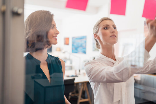 Smiling businesswoman looking at female colleague working in office seem through glass