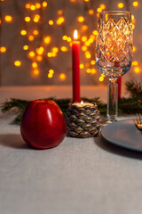 Christmas festive table served with grey plate, red candle, red apple and fir tree branch on garland lights background