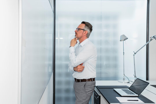 Businessman with hand on chin contemplating while looking at whiteboard in office
