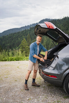 Smiling mature man packing bag while standing by car