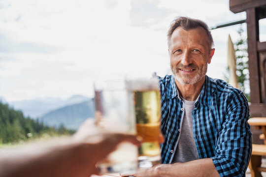 Smiling man toasting beer glass with friend at bar