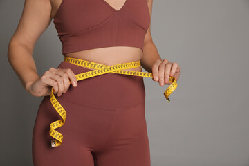 Woman measuring waist with tape on grey background, closeup