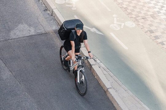 Young Female Essential Worker Carrying Backpack Riding Cycle On Road