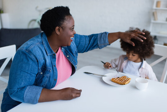 Happy African American Granny Touching Curly Hair Of Granddaughter Eating Waffle For Breakfast