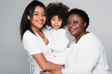african american girl in hands of happy mom and granny looking at camera isolated on grey