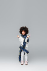 full length view of cheerful african american girl in white clothes posing with christmas tinsel on...