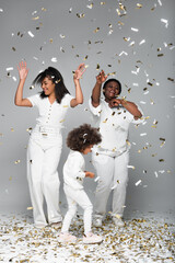 happy african american women and child in white clothes under shiny confetti on grey