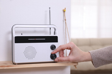 Woman turning volume knob on radio at home, closeup