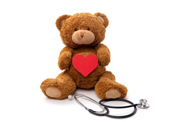medicine, healthcare and childhood concept - teddy bear toy with stethoscope holding red heart on white background