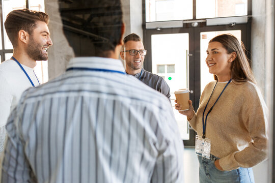 business, people and corporate concept - group of happy smiling colleagues with name tags drinking takeaway coffee at office