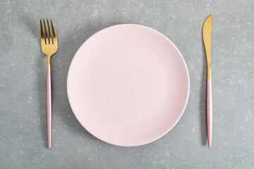 Pink plate and gold cutlery on gray kitchen table. Flat lay, top view, copy space