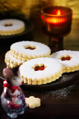 Linzer cookies served on dark plate, Christmas glass decoration and burning candle. Dark wooden table, golden backdrop, warm light, high resolution
