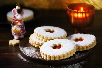 Linzer cookies served on dark plate, Christmas glass decoration and burning candle. Dark wooden table, golden backdrop, warm light, high resolution
