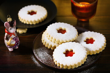 Linzer cookies served on dark plate, Christmas glass decoration and burning candle. Dark wooden table, golden backdrop, warm light, high resolution
