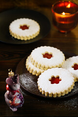 Linzer cookies served on dark plate, Christmas glass decoration and burning candle. Dark wooden table, golden backdrop, warm light, high resolution