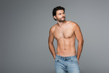 good-looking and muscular man in jeans looking awat isolated on grey