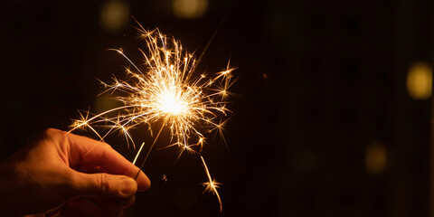 Hand holding sparkler. Merry Christmas and New year party light over night sky.