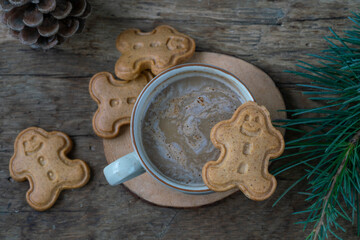 coffee and gingerbread man shaped cookies on wooden table decorated with pine tree branches for Christmas or new year. 