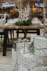 Gift boxes near table decorated for christmas dinner. Xmas presents in white, silver and green color palette. 
