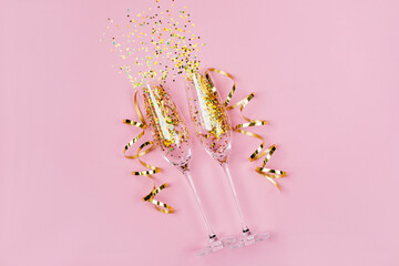 Two glasses of champagne with shiny golden confetti lying on pink background with copy space for...