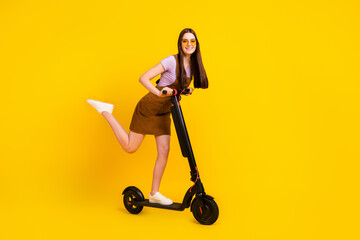 Full length body size view of attractive cheerful girl riding scooter good mood isolated over bright yellow color background © deagreez