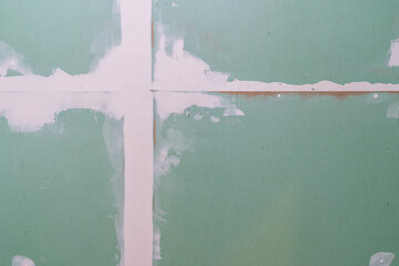 Fragment of a green plasterboard wall at the time of construction or renovation. Filled, criss-crossing seams are visible. Texture.