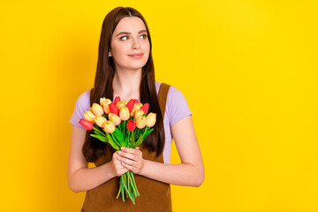 Portrait of attractive brown-haired girl holding in hands flowers copy space isolated over bright yellow color background