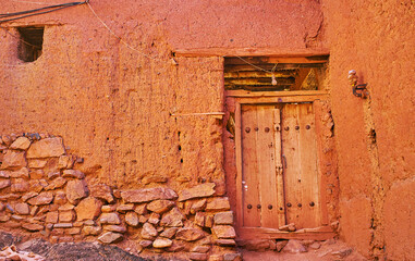 The old house wall, built partly of stone and earthen brick and covered with reddish adobe,...