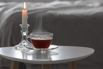 glass cup of tea  with burning candle  on white table in bedroom