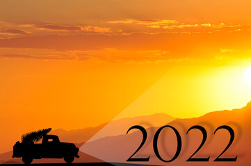 Fototapeta na wymiar the concept of the new year, the silhouette of a car with a Christmas tree in the back of a truck lights up the figures 2022