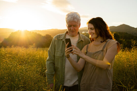 Smiling daughter showing mobile phone to father in field