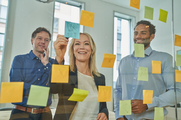 Smiling businesswoman writing on adhesive note while discussing with male colleagues in board room