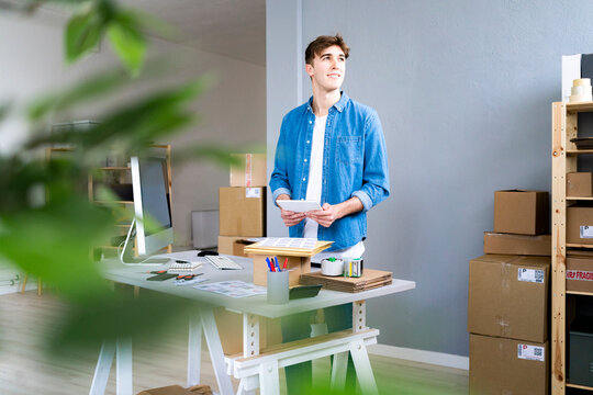 Smiling businessman looking away while holding digital tablet in office