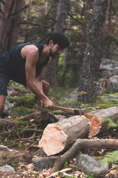 Young man cutting fallen tree trunk with axe in forest