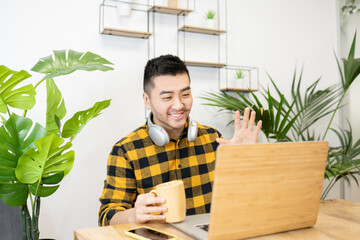 Smiling young male professional waving while doing video call through laptop in office