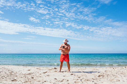 Shirtless gay man using mobile phone at beach during vacation