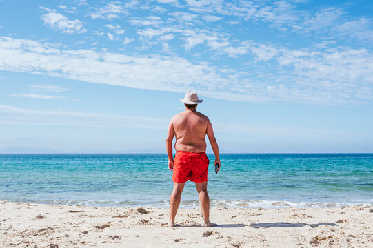 Overweight man in hat looking at sea on sunny day