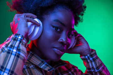 Close-up happy young girl, student listening to music in headphones isolated on dark green studio...